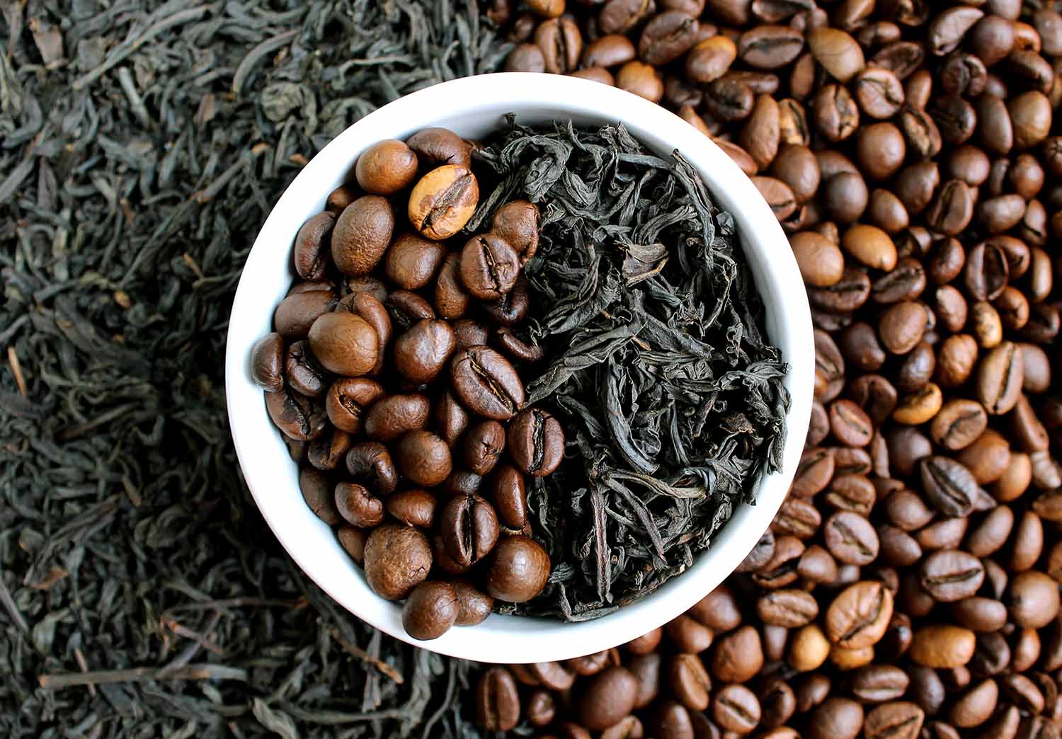 Coffee beans and black tea leaves in a white bowl